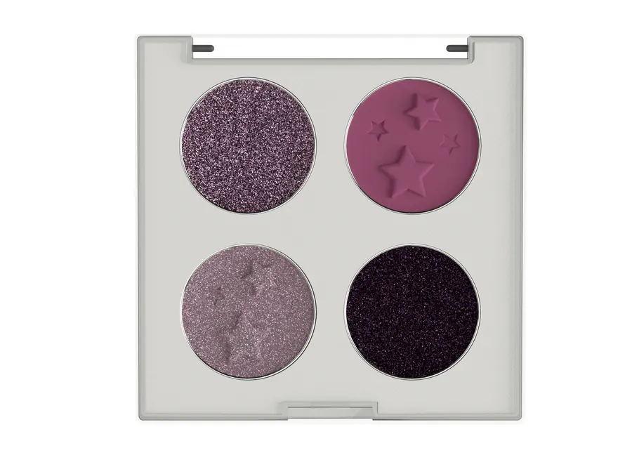An open white compact photographed from directly above, holding four round eyeshadow pans in purple shades, two glittery, one matte plum embossed with stars and one pale shimmer.
