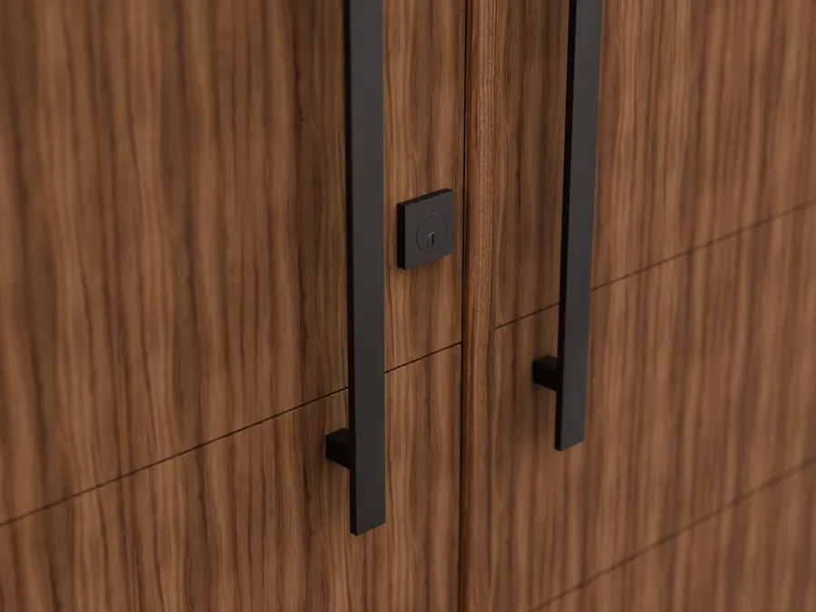 Close angled view of two walnut doors meeting at the center, each fitted with a long matte black square bar pull, with a square black deadbolt escutcheon on the left door.