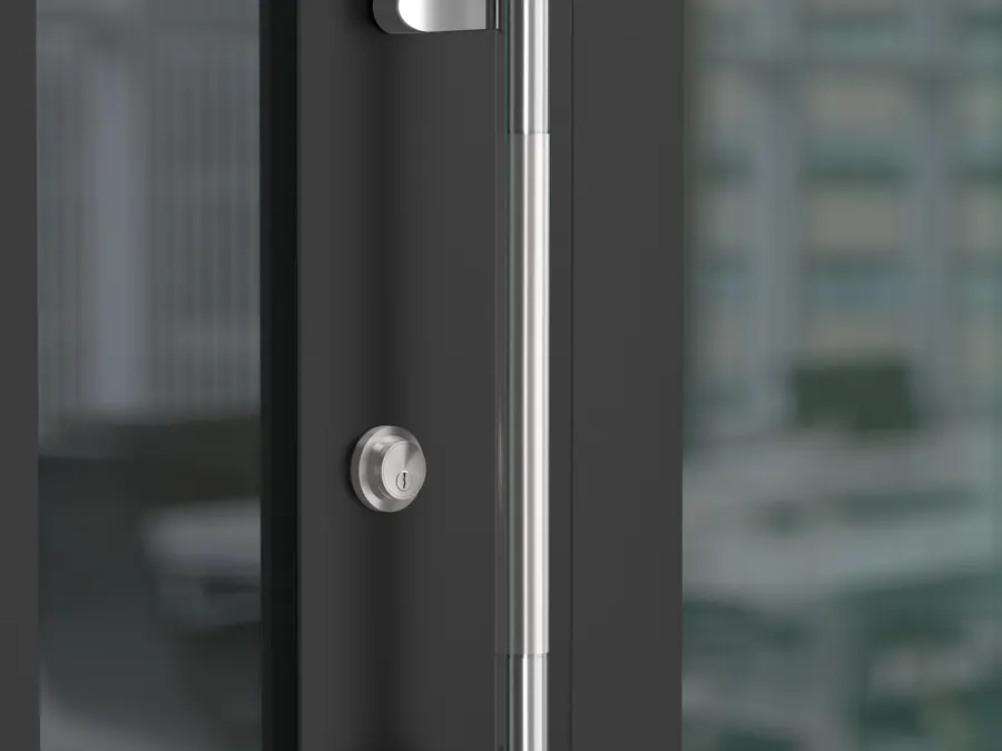 Offset stainless pull and round lock rose on a dark framed glass office door, with a blurred open plan office behind.