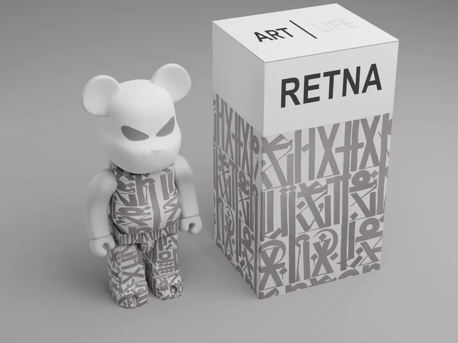 A white toy bear figure with an angular scowling face, its body printed with grey angular graffiti letterforms, standing beside a matching tall white and grey box on a grey background.
